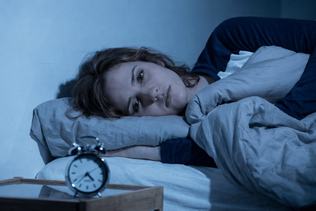 Anxious Woman lying awake in bed at night, staring at the ceiling with an alarm clock on the bedside table, conveying work stress, insomnia and mental exhaustion.