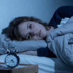 Anxious Woman lying awake in bed at night, staring at the ceiling with an alarm clock on the bedside table, conveying work stress, insomnia and mental exhaustion.